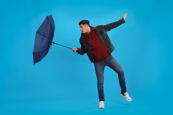 Man with umbrella caught in gust of wind on light blue background - Foto, Imagen