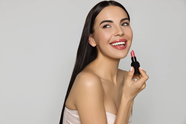 Young woman with beautiful makeup holding glossy lipstick on light gray background - Φωτογραφία, εικόνα