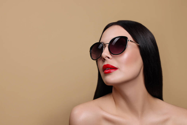 Attractive woman in fashionable sunglasses against beige background. Space for text - Zdjęcie, obraz