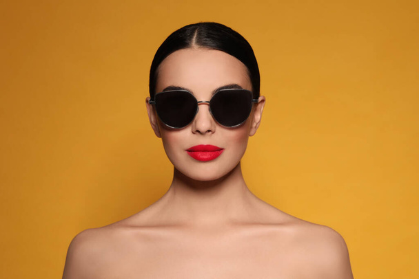 Attractive woman in fashionable sunglasses against orange background - Фото, изображение