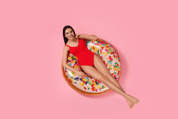 Young woman in stylish swimsuit on inflatable ring against pink background, top view - Foto, immagini