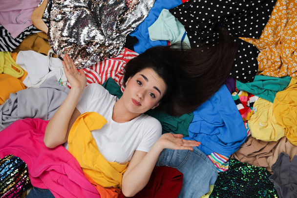 Young woman with lots of clothes on floor in room, top view. Fast fashion - Fotografie, Obrázek