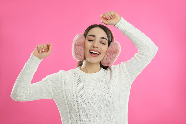 Beautiful young woman wearing earmuffs on pink background - Foto, imagen