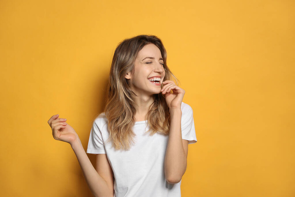 Cheerful young woman laughing on yellow background - Фото, зображення