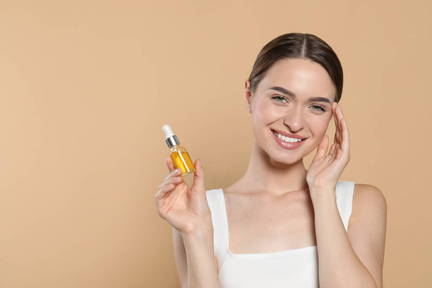 Young woman with bottle of essential oil on beige background, space for text - 写真・画像
