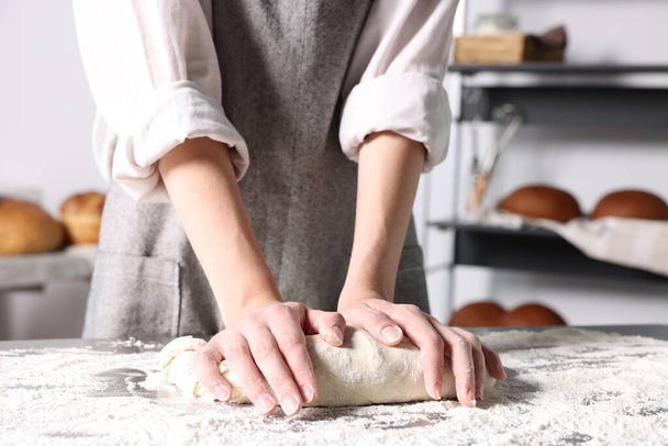 Woman kneading dough at table in kitchen, closeup - Fotó, kép
