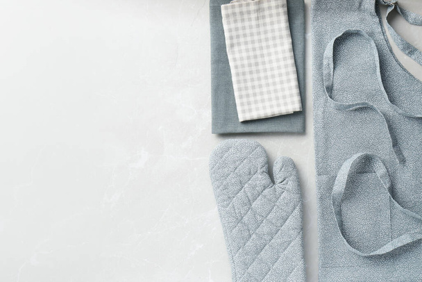 Kitchen napkins, apron and glove on light marble table, flat lay. Space for text - 写真・画像