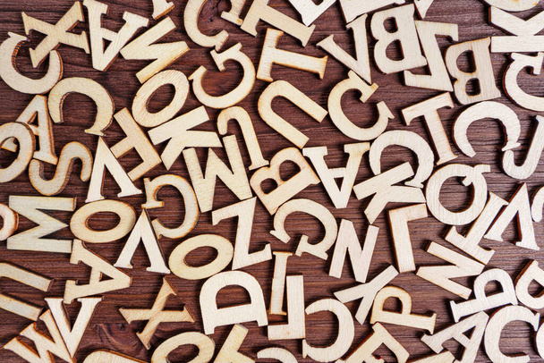 Abstract background made from scattered wooden letter characters on a dark wooden table. - Foto, Bild