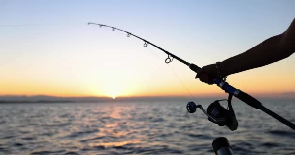 Une main avec une canne à pêche sur fond d'un beau coucher de soleil sur l'eau, gros plan. Concept de pêche en bateau - Séquence, vidéo