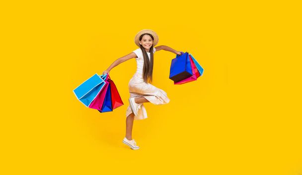 happy teen girl running with shopping bags on yellow background. full length. - Fotografie, Obrázek