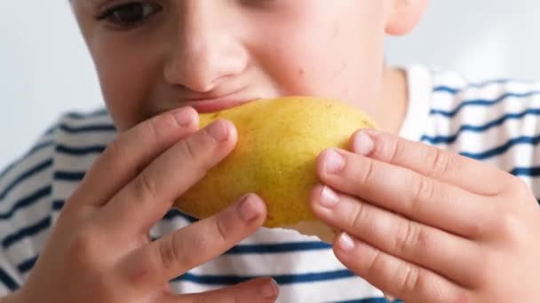 Ένα μικρό αγόρι τρώει ένα ζουμερό αχλάδι και κοιτάζει την κάμερα. Ώριμα φρούτα - Πλάνα, βίντεο
