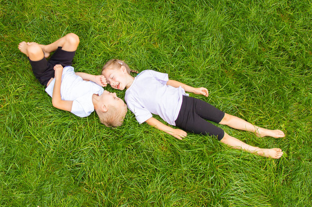 子供たちは芝生の上に横たわって空を見ています。6歳の男の子と女の子、ヨーロッパの外観は、異なるポーズで緑のガスに横たわっています. - 写真・画像