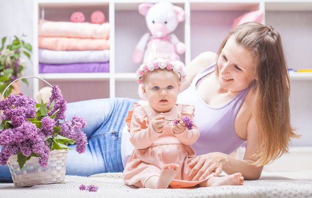 mother with a little daughter with a bouquet of lilacs in the childrens room - Photo, Image