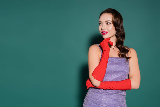happy young woman in red gloves and purple dress looking away on green - Photo, Image