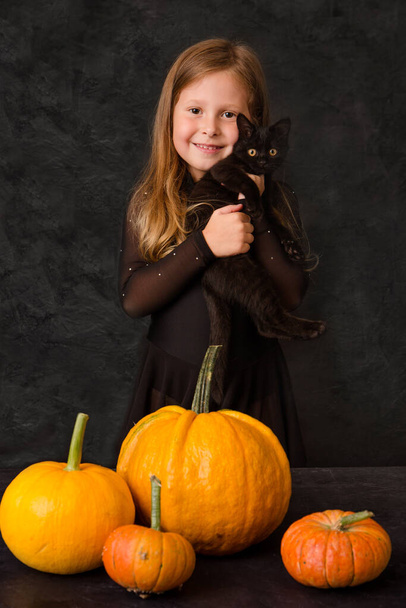 Ein kleines Mädchen mit einer schwarzen Katze auf schwarzem Hintergrund - Foto, Bild