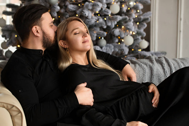 Ein schöner Mann und eine schwangere Frau an Weihnachten am Kamin - Foto, Bild