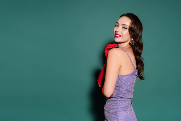 charming young woman in red gloves and purple dress smiling on green background  - Fotoğraf, Görsel