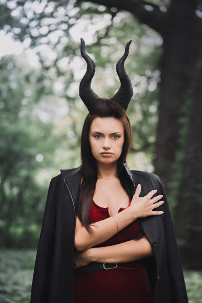 Beautiful woman with long black horns in the forest. Halloween concept - Photo, image