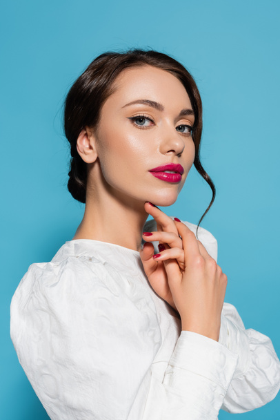 portrait of brunette young woman in white blouse looking at camera isolated on blue - Foto, imagen
