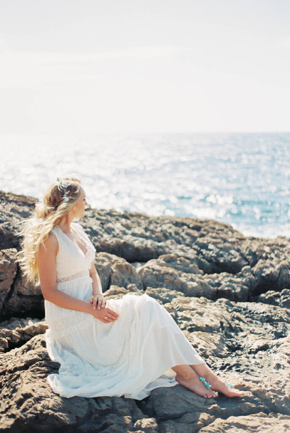 Босонога наречена сидить на скелях і дивиться на блискуче море. Високоякісна фотографія
 - Фото, зображення