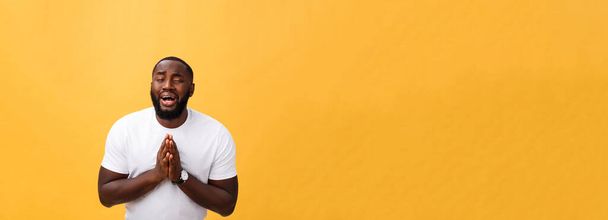 Estúdio retrato do jovem afro-americano de camisa branca, de mãos dadas em oração, olhando para a câmera com expressão cética pensativa em seu rosto, suspeitando de algo. Linguagem corporal
 - Foto, Imagem