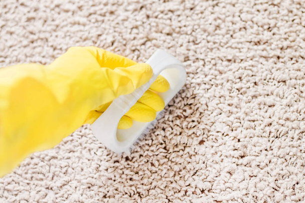 Una mano femenina en un guante amarillo sostiene un cepillo y lava la alfombra. Limpieza de alfombras - Foto, imagen