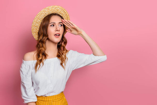 Surprised girl in a straw hat looks away, isolated on a pink background, copy space. A young woman in summer clothes is looking for discounts. The girl is shocked by the summer sales - Fotoğraf, Görsel