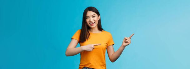 Upbeat friendly asian cute girl with dark haircut lively pointing left introduce awesome new copy space, smiling broadly toothy happy grin, stand blue background joyful, recommend link. - Фото, зображення