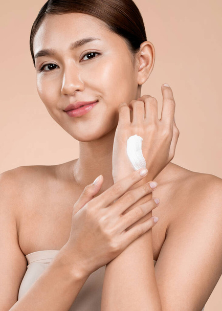 Closeup ardent girl with soft makeup looking at camera, applying moisturizing skincare cream on her hand, isolated background. Skincare cream applied by female model concept. - Fotó, kép