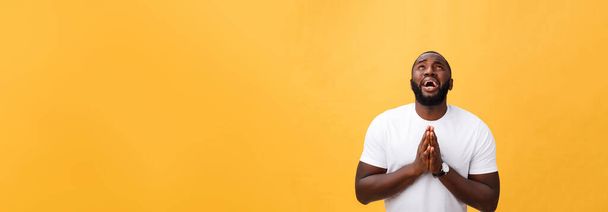 Studio portrait of young African American man in white shirt, holding hands in prayer, looking at the camera with thoughtful skeptical expression on his face, suspecting of something. Body language - Photo, Image