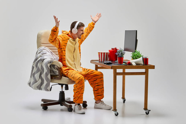 Angry young man in amazing costume of tiger sitting at computer desk at home isolated over gray background. Art, ideas, creativity, working and holidays concept - Φωτογραφία, εικόνα