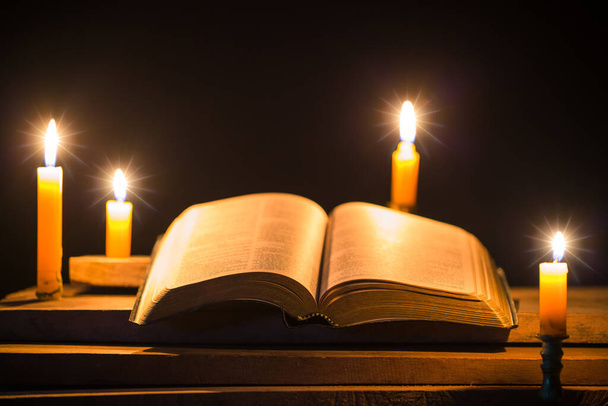 Light candle with holy bible and cross or crucifix on old wooden background in church.Candlelight and open book on vintage wood table christianity study and reading in home.Concept of christ religion - Fotografie, Obrázek