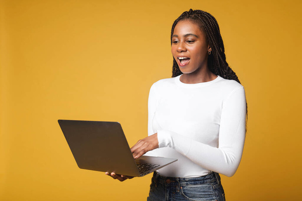 Happy excited African American female student cannot believe her eyes, opened her mouth, standing with open laptop and checking grades, feeling happy from passing the exam, victory concept - Fotografie, Obrázek