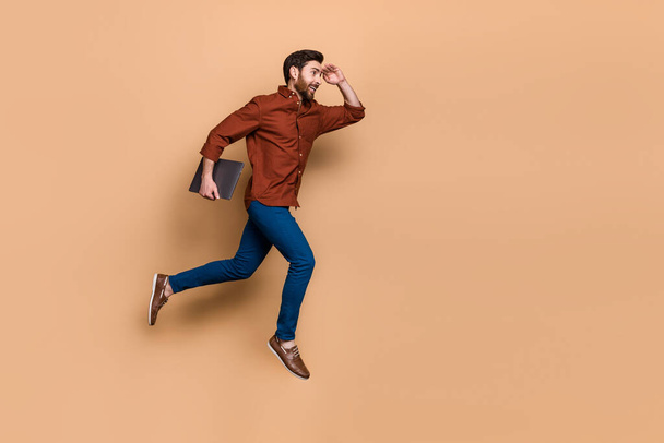 Full body portrait of energetic handsome guy jump run hand touch forehead look empty space isolated on beige color background. - 写真・画像