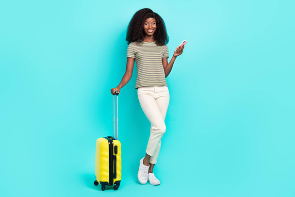 Full size portrait of cheerful nice girl hand hold telephone suitcase isolated on shiny turquoise color background. - Foto, imagen