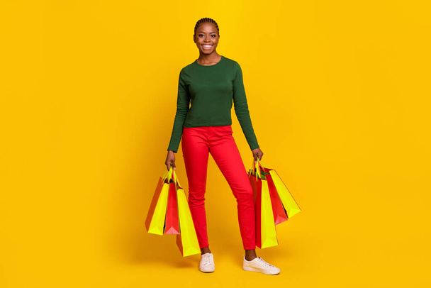 Full length photo of adorable sweet woman wear green shirt holding shoppers isolated yellow color background. - Zdjęcie, obraz