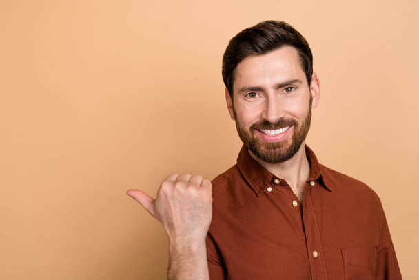 Portrait of cheerful nice person indicate thumb finger empty space isolated on beige color background. - Foto, Imagen