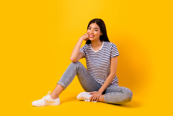 Full size photo of adorable satisfied filipino lady sit floor arm touch cheek toothy smile isolated on yellow color background. - Foto, Imagem