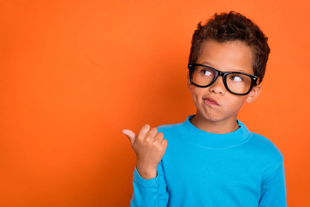 Photo portrait of charming little pupil boy point empty space specs unsure wear trendy blue clothes isolated on orange color background. - Foto, afbeelding