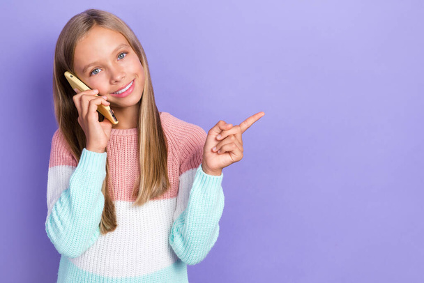 Foto von fröhlichen kleinen Mädchen sprechen Gerät Hand zeigen leeren Raum empfehlen Angebot Gadget 4g-Verbindung isoliert auf lila Hintergrund. - Foto, Bild