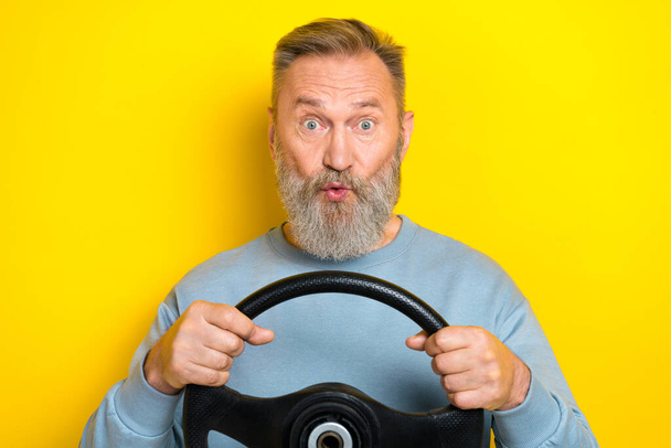 Photo of excited funky man pensioner dressed blue pullover big eyes riding auto isolated yellow color background. - Fotografie, Obrázek