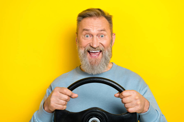 Photo of charming excited man pensioner dressed blue pullover open mouth riding auto isolated yellow color background. - Foto, Imagem