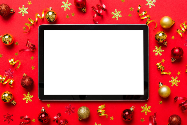 Kerstmis online winkelen van thuis tablet pc met blanco witte display bovenaanzicht. Tafel met kopieerruimte op gekleurde achtergrond met kerstversieringen ballen,. Winter vakantie verkoop achtergrond. - Foto, afbeelding