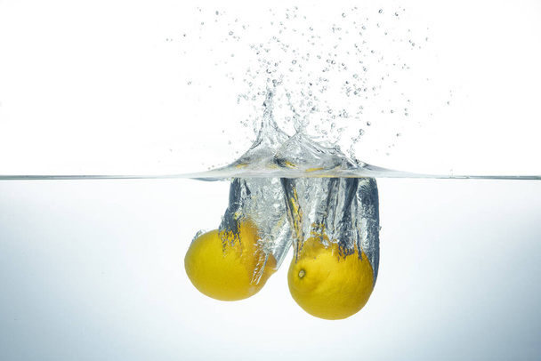Two lemons splashing in clear water. Side view on white background. - Foto, Imagem