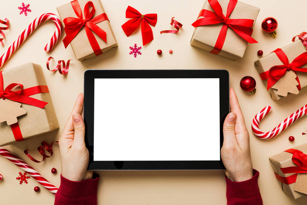 Karácsonyi online vásárlás otthonról, női kéz tartja tabletta pc üres fehér kijelző felső nézet. nő kézfogás tabletta üres képernyőn, karácsonyfa és ajándékok a háttérben. - Fotó, kép