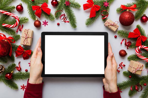 Boże Narodzenie zakupy online z domu, ręce kobiet trzymając tablet z pustym białym wyświetlaczem widok z góry. kobieta ręka gospodarstwa tabletki z pustym ekranem, choinka i prezenty na tle. - Zdjęcie, obraz