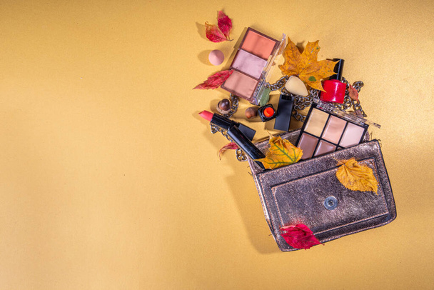 Otoño maquillaje conjunto sobre fondo de mesa de oro, con hojas de otoño y accesorios de belleza. Varios cosméticos profesionales de maquillaje sombras, lápiz labial, corrector, rimel, delineador de ojos, bronceador, rubor - Foto, imagen