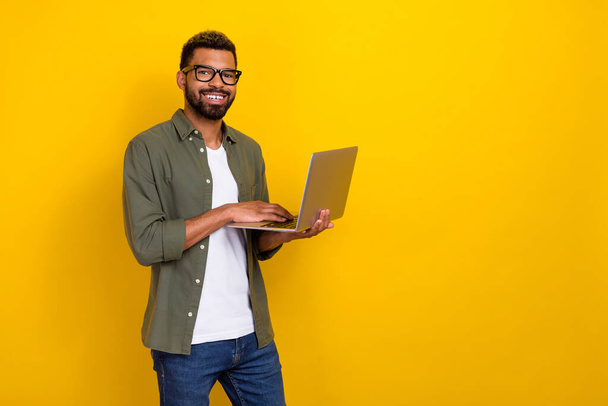 Photo of pretty confident man wear khaki shirt spectacles typing modern device empty space isolated yellow color background. - Fotografie, Obrázek