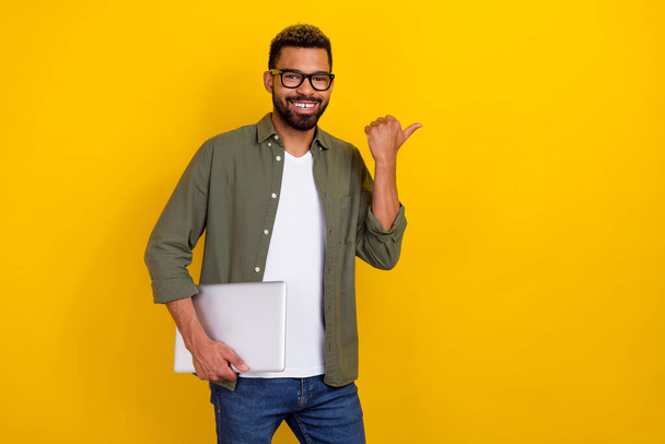 Photo of pretty good mood man wear khaki shirt hand spectacles holding modern device empty space isolated yellow color background. - 写真・画像