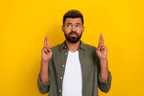 Photo of doubtful unsure man wear khaki shirt fingers crossed looking empty space isolated yellow color background. - Fotografie, Obrázek